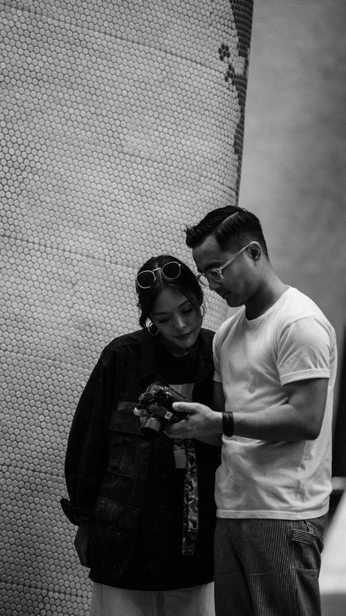 Two friends share a moment, reviewing a camera screen in a candid black and white photo.
